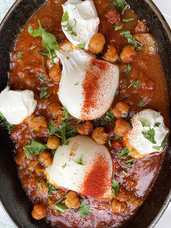 一锅地中海健康早餐的特写图片:shakshouka / shakshuka / chakchouka，鹰嘴豆，鸡蛋在番茄，辣椒，洋葱，橄榄油和大蒜的酱汁中水煮，上面放着香菜，俯瞰